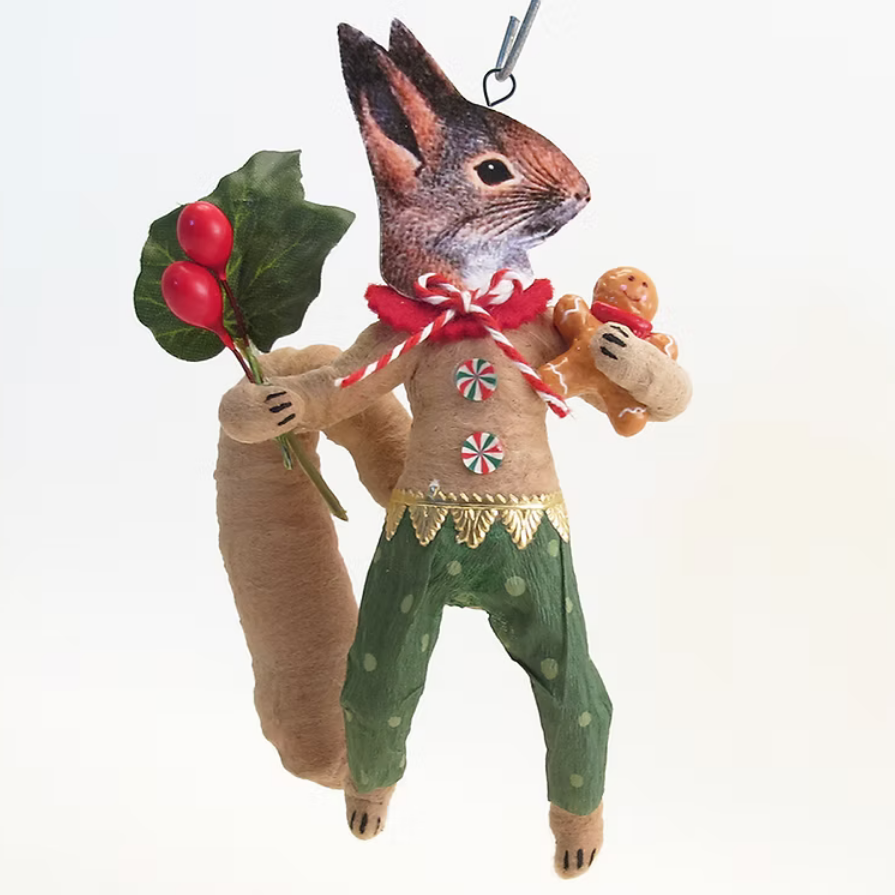 A handmade felt rabbit Christmas ornament with a brown body, green pants, a red bow, and a gingerbread cookie, holding a sprig of holly on a white background.