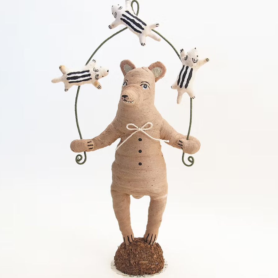 A handmade cotton figurine of a bear holding a wire hoop with four small striped dog toys, set against a plain white background.