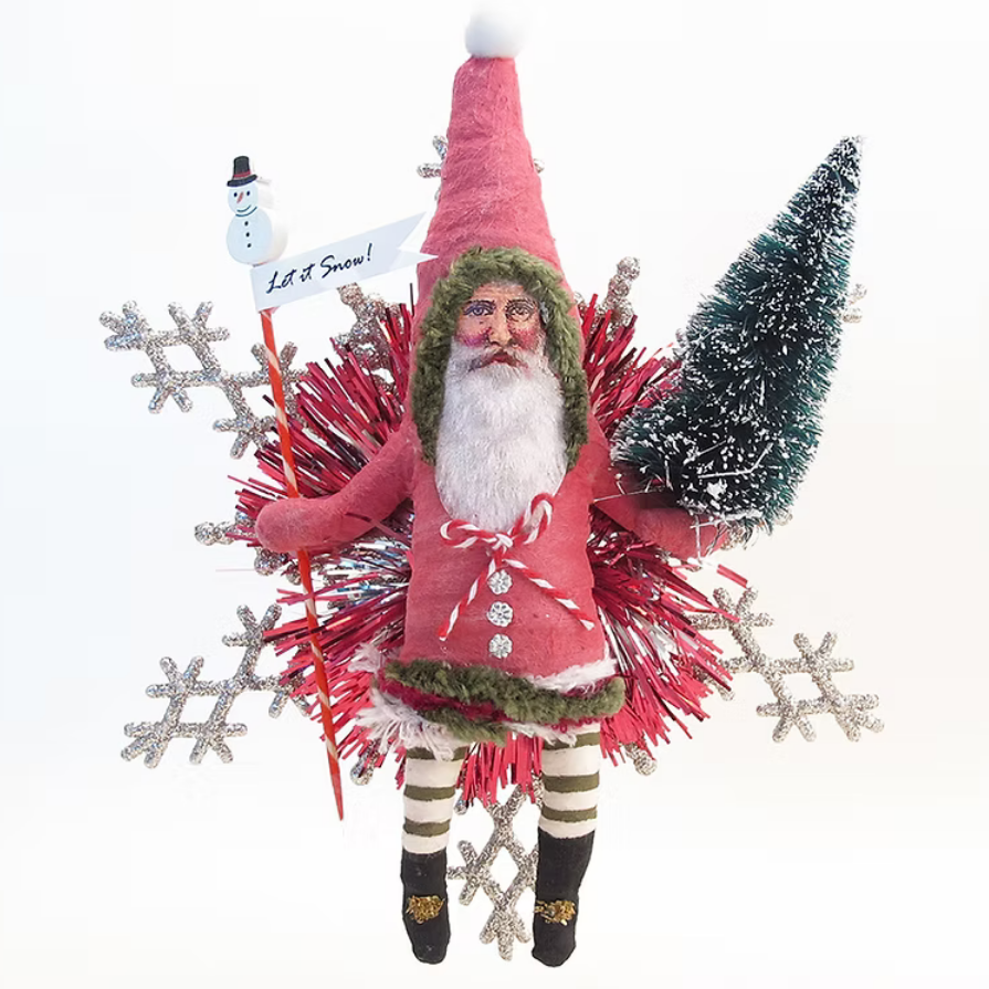 A festive Christmas hanging ornament featuring a plush Santa Claus figure in a pink suit and green hat, surrounded by red tinsel, silver glitter snowflakes, a small green tree, and a snowman sign that reads 'Let It Snow!'.