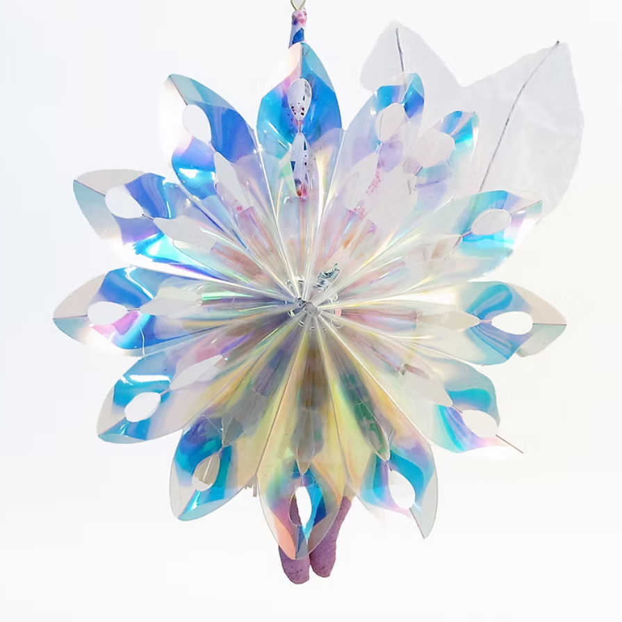 An iridescent hanging ornament made from layered translucent plastic bags, featuring a starburst design with blue, purple, and pink reflective tones against a white background.