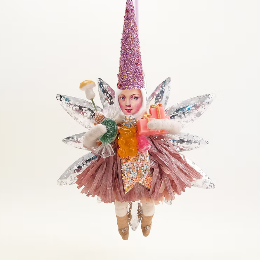 A whimsical handmade fairy ornament hanging against a plain white background. The ornament features a small painted face, a tall glittery pink cone hat, silver sequined wings, a pink tulle skirt, and a yellow-orange bodice decorated with colorful glitter and candy-like accents.