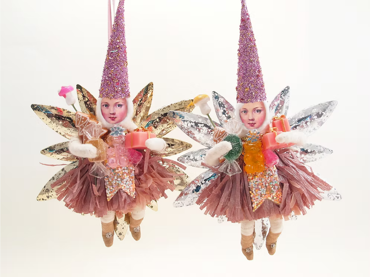 Two hanging fairy ornaments with glittery pink pointed hats, multicolored wings, and sparkly pink skirts, each holding small gift boxes, shown against a plain white background.