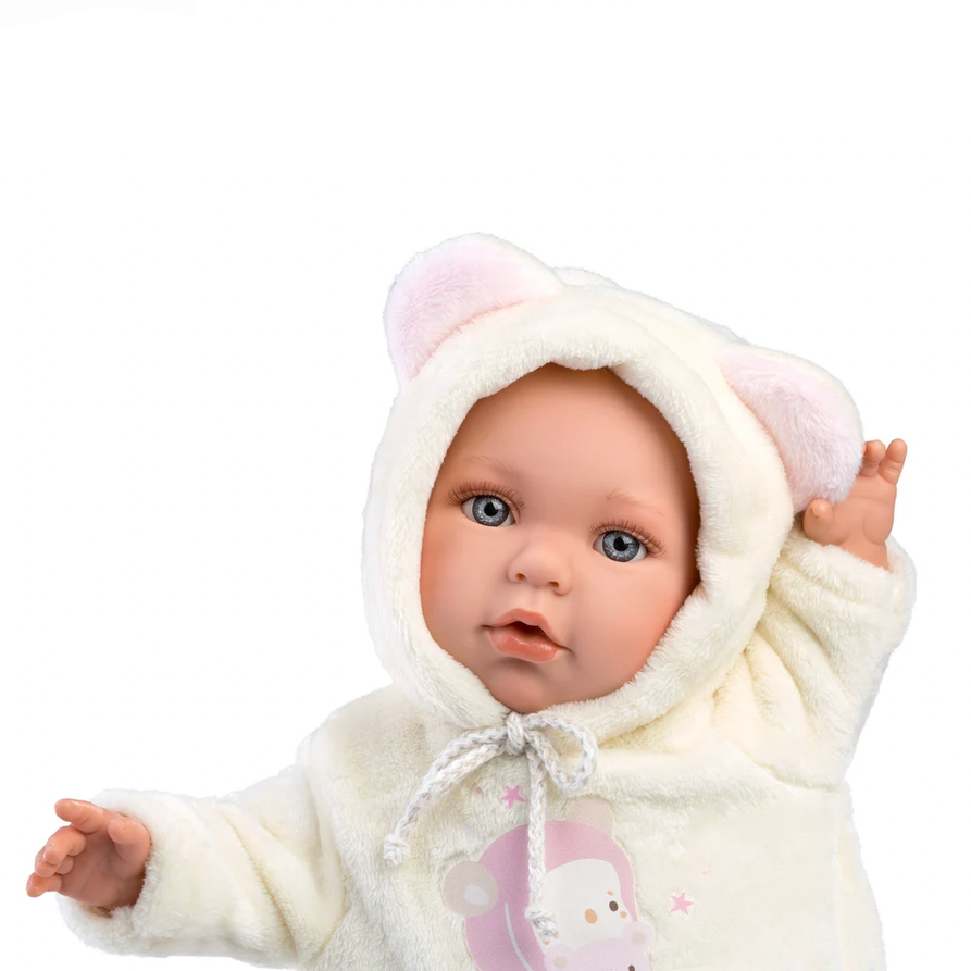 A baby doll or realistic baby toy wearing a cream hooded fleece outfit with pink bear ears and a pink cartoon graphic on the front, shown on a product listing page.