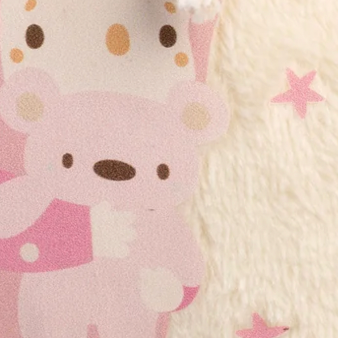 A close-up of a plush fabric item featuring a pink cartoon bear character and a white rope tassel, next to a cream-colored fuzzy background with pink star accents.