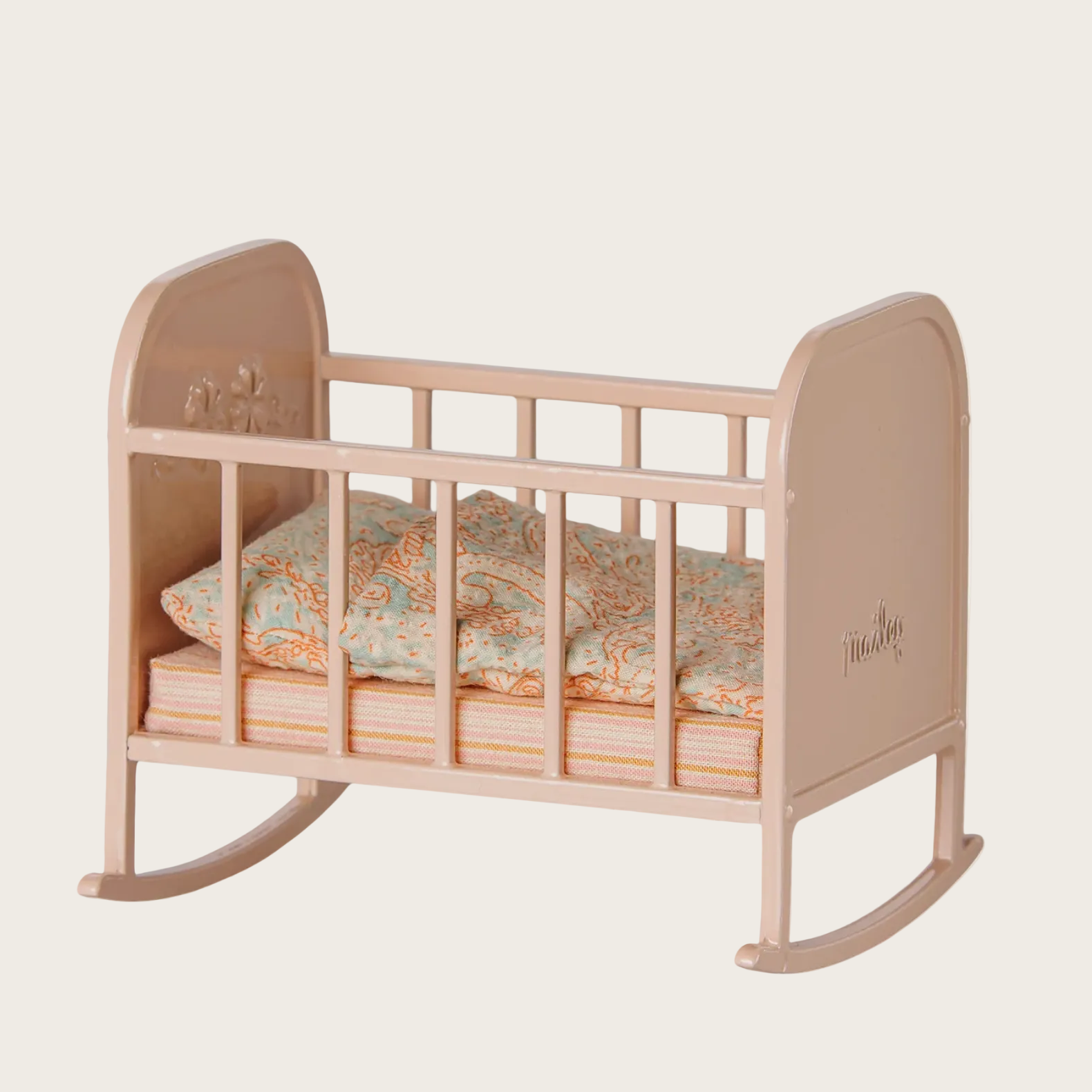 A light pink wooden baby crib with a matching quilted pillow, shown on a white webpage background with the Maileg brand logo visible.