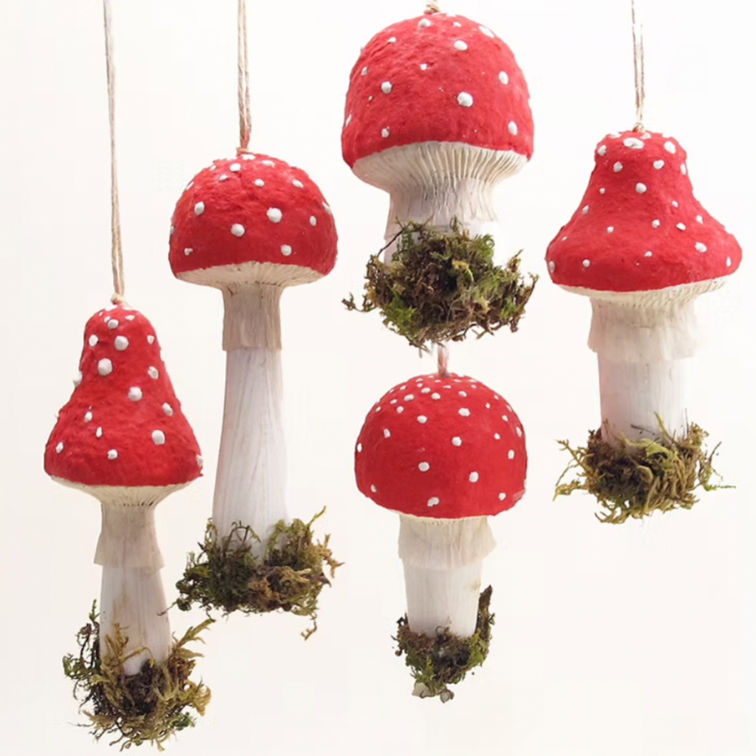 Five red and white mushroom-shaped hanging ornaments with white stems and green moss at the base, shown against a plain white background.