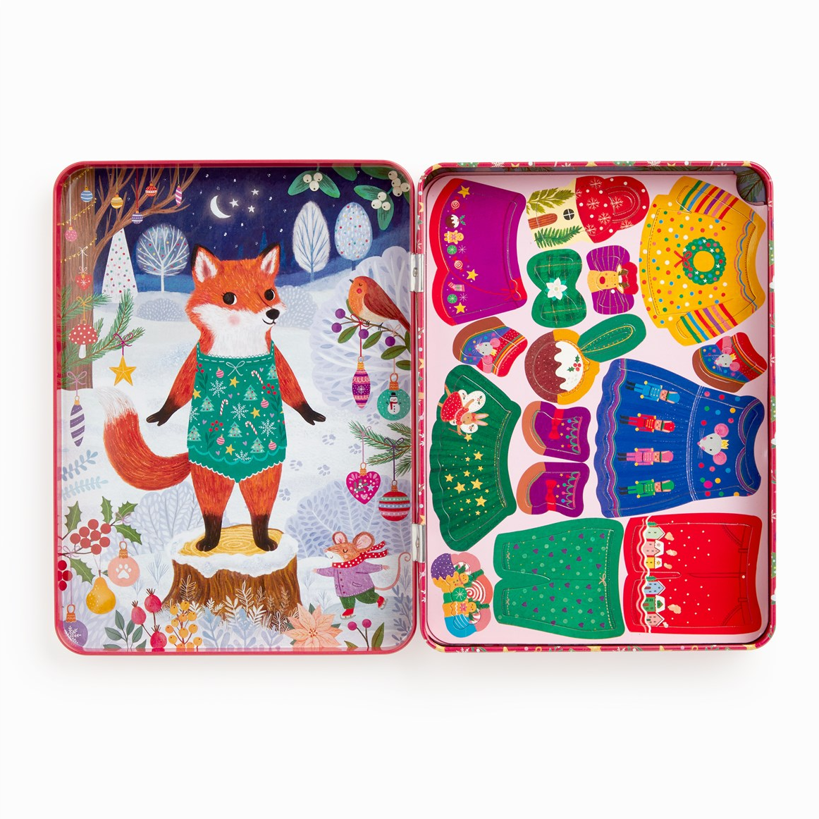 A festive Christmas-themed wooden toy set in an illustrated tin, shown open to reveal colorful wooden sweaters and accessories on the right, and a winter forest scene with a fox on the left.