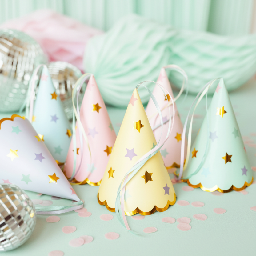 A screenshot of a Shopify browser window showing a product image of pastel party hats with gold star accents. The party hats are light blue, pink, and pale yellow, decorated with gold stars and scalloped edges, set against a light pastel background with party confetti and ribbons.
