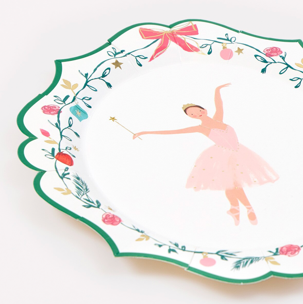 A scalloped white plate with a festive fairy tale theme, featuring a ballerina in a pink tutu and a decorative border of green leaves, red berries, and a pink bow.