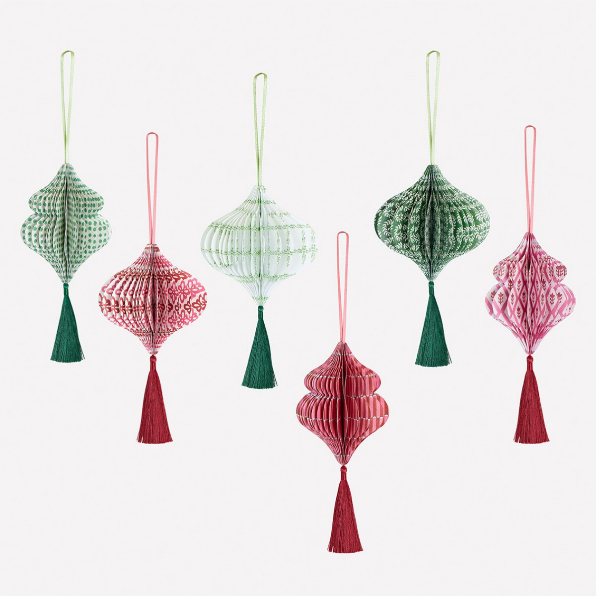 Six hanging decorative lanterns made of patterned tissue paper in green and pink tones, each with a tassel, arranged on a plain light background.