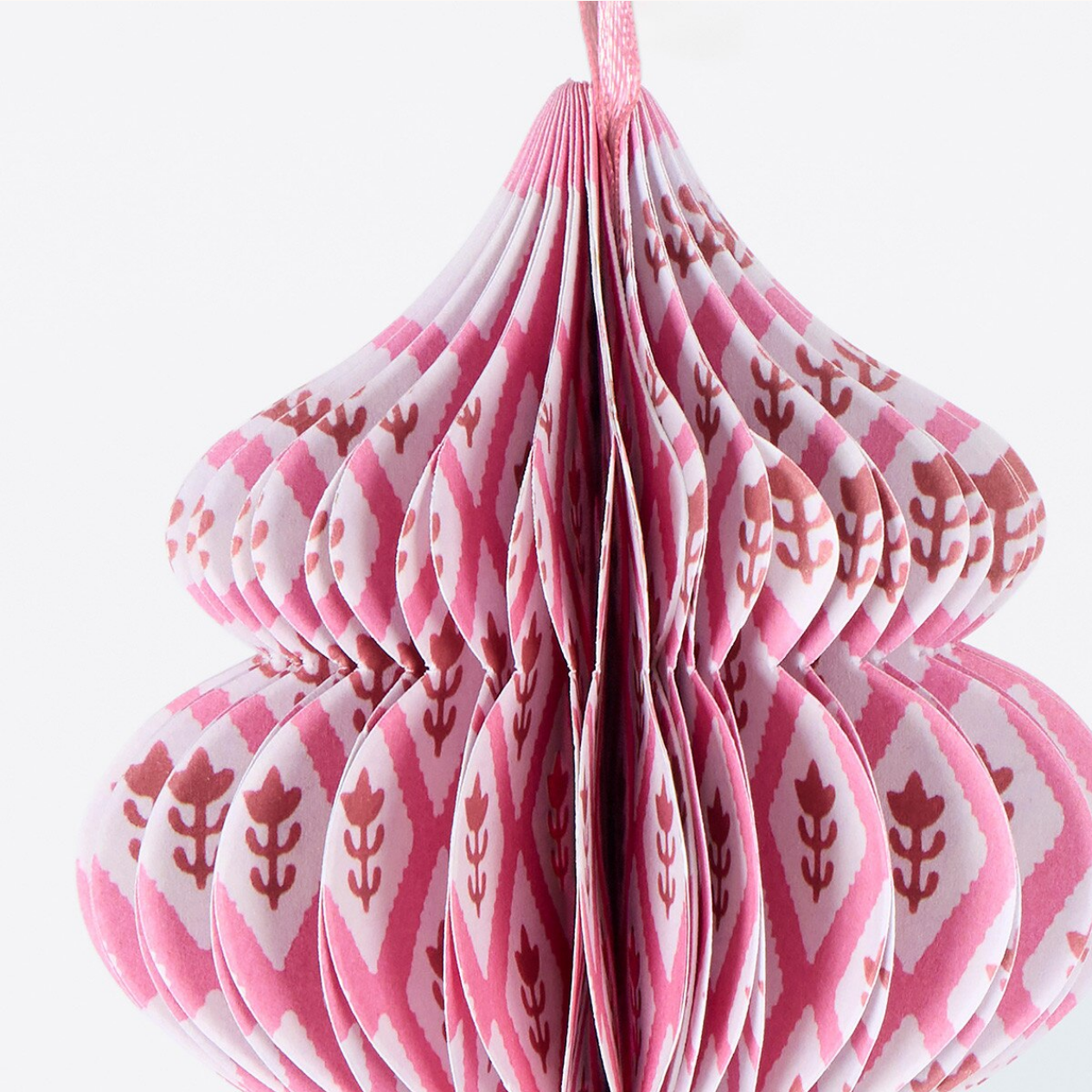 Pink and white patterned paper honeycomb hanging ornament with a floral ikat design, shown against a plain white background.