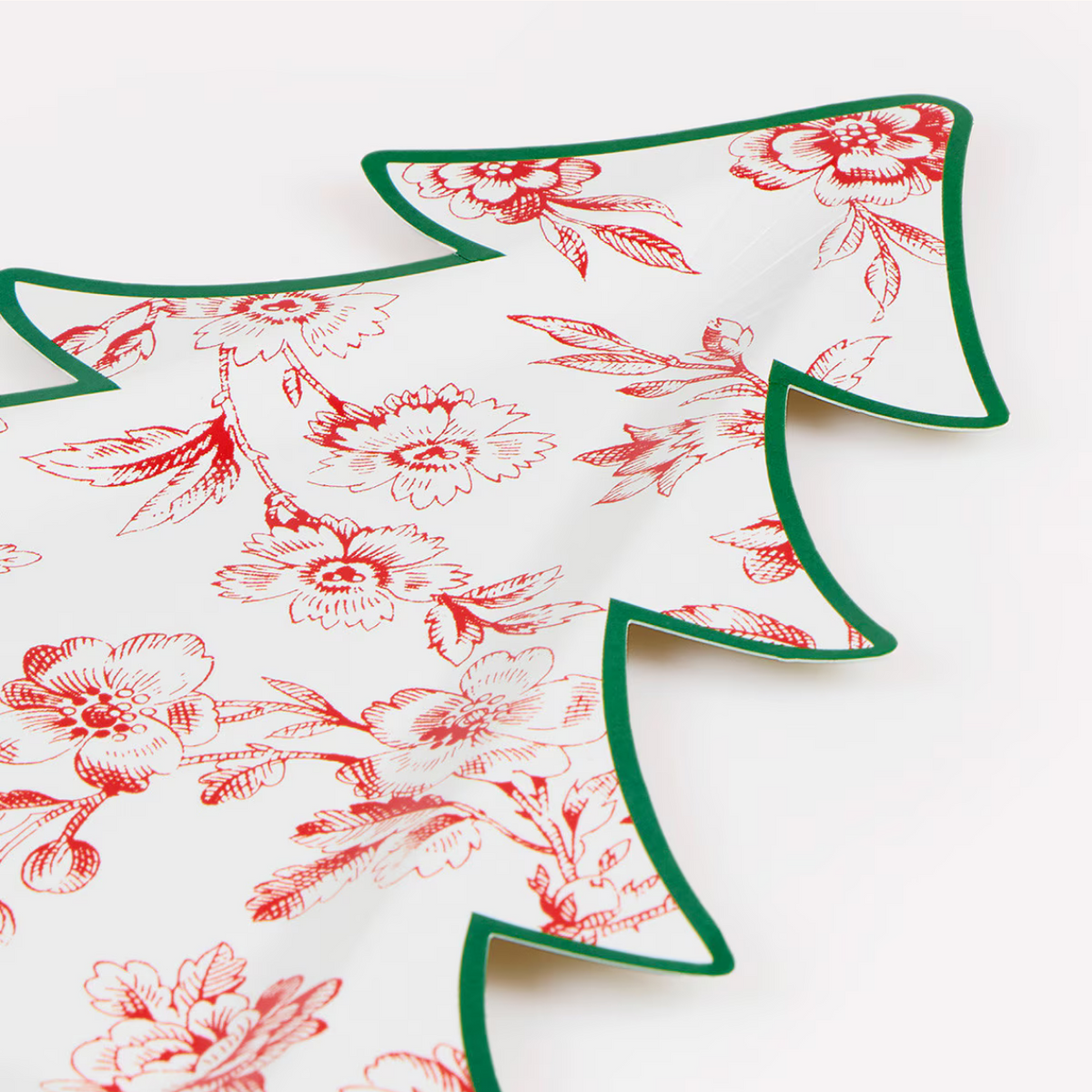 A close-up of a white paper napkin with a red floral toile pattern and a green scalloped edge, folded to show its shape and texture.