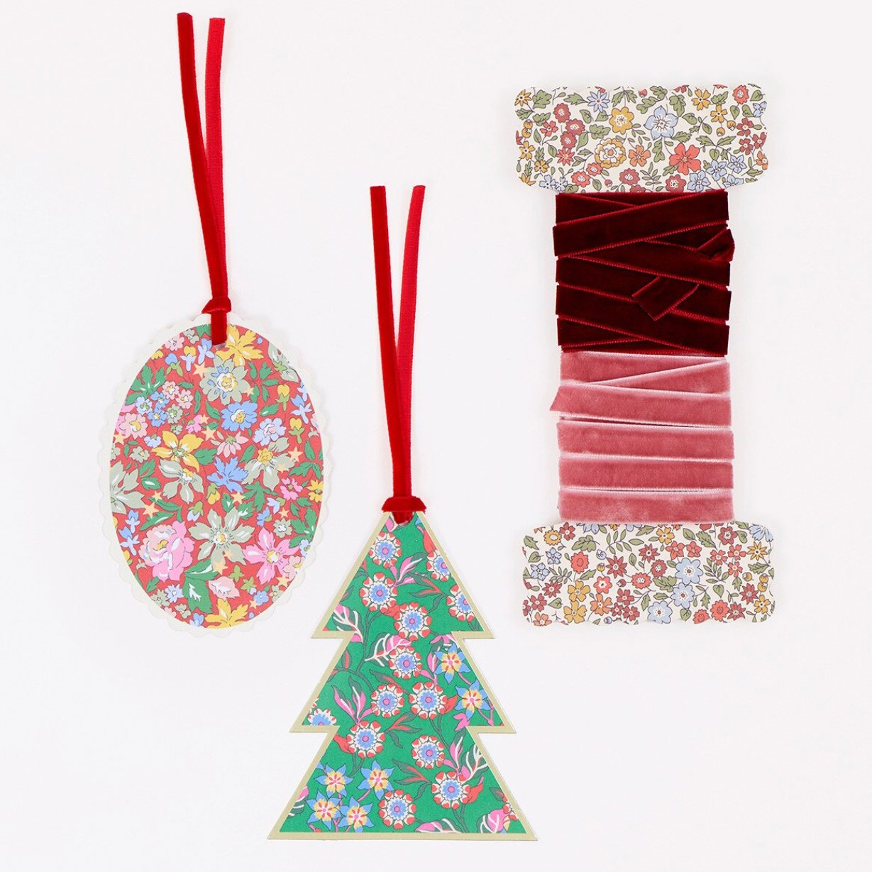 Two decorative hanging ornaments on a plain white background: an oval ornament with a multicolor floral print and red hanging ribbon, and a tree-shaped ornament with a green floral print and red hanging ribbon. A third floral fabric swatch is shown to the right.