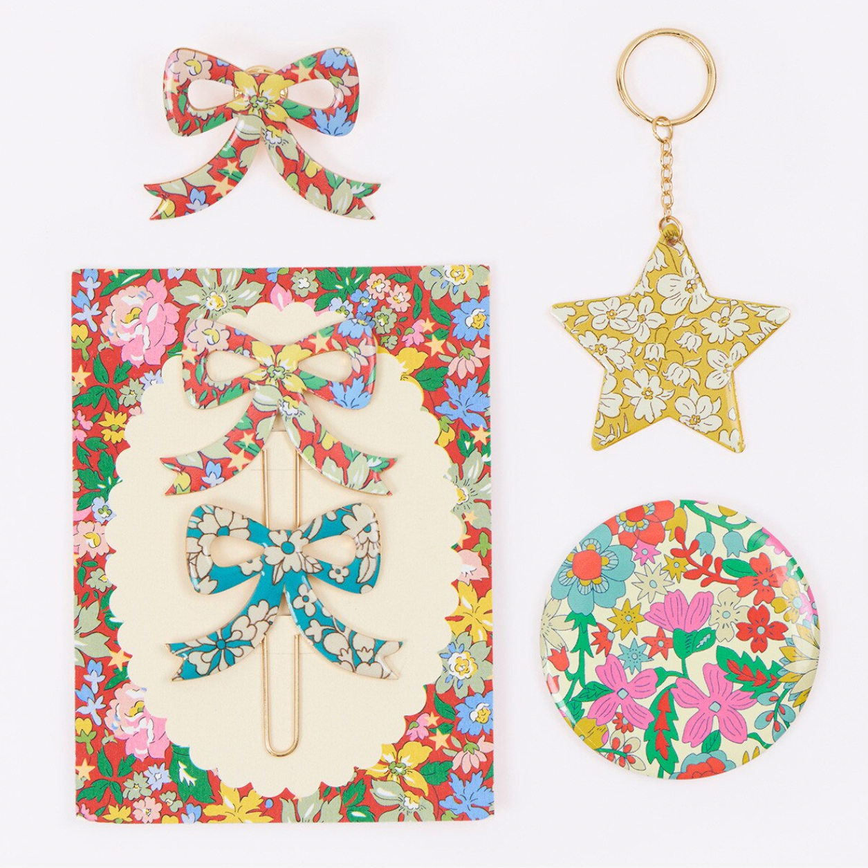 A flat lay of floral paper goods on a white background, including a bow-shaped paper clip, a star-shaped keychain, a round paper weight, and a decorative sheet with a bow-shaped pins.
