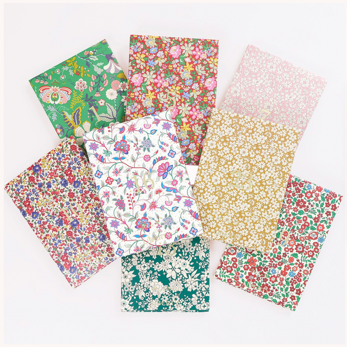 Eight square fabric swatches with various floral and botanical patterns in green, pink, red, yellow, and white, arranged in a fan-like layout on a white background.