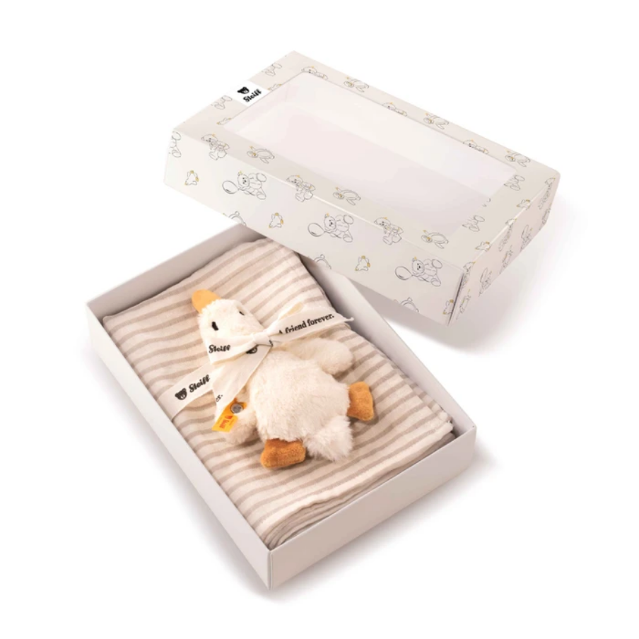 A baby gift set in a white box with a clear window lid, containing a plush white duck toy tied with a white ribbon and folded cream-and-beige striped fabric.
