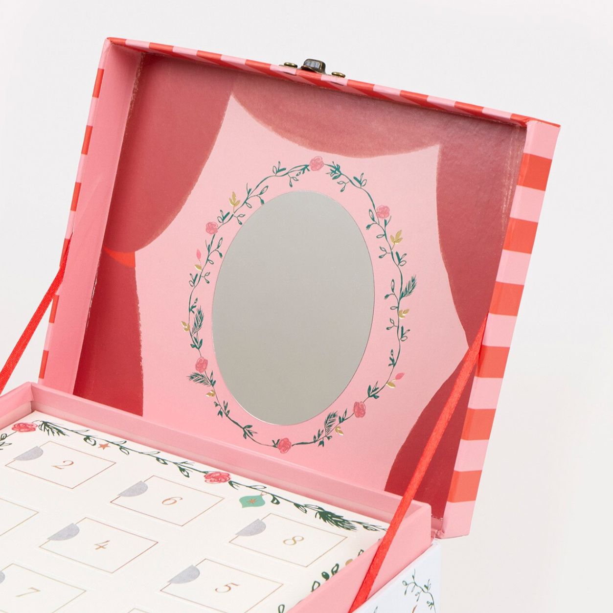 An open decorative gift box with a pink interior, a round mirror framed by a floral wreath, and numbered gift cards visible at the bottom. The exterior has pink and white stripes with red ribbon ties, photographed on a clean white background.