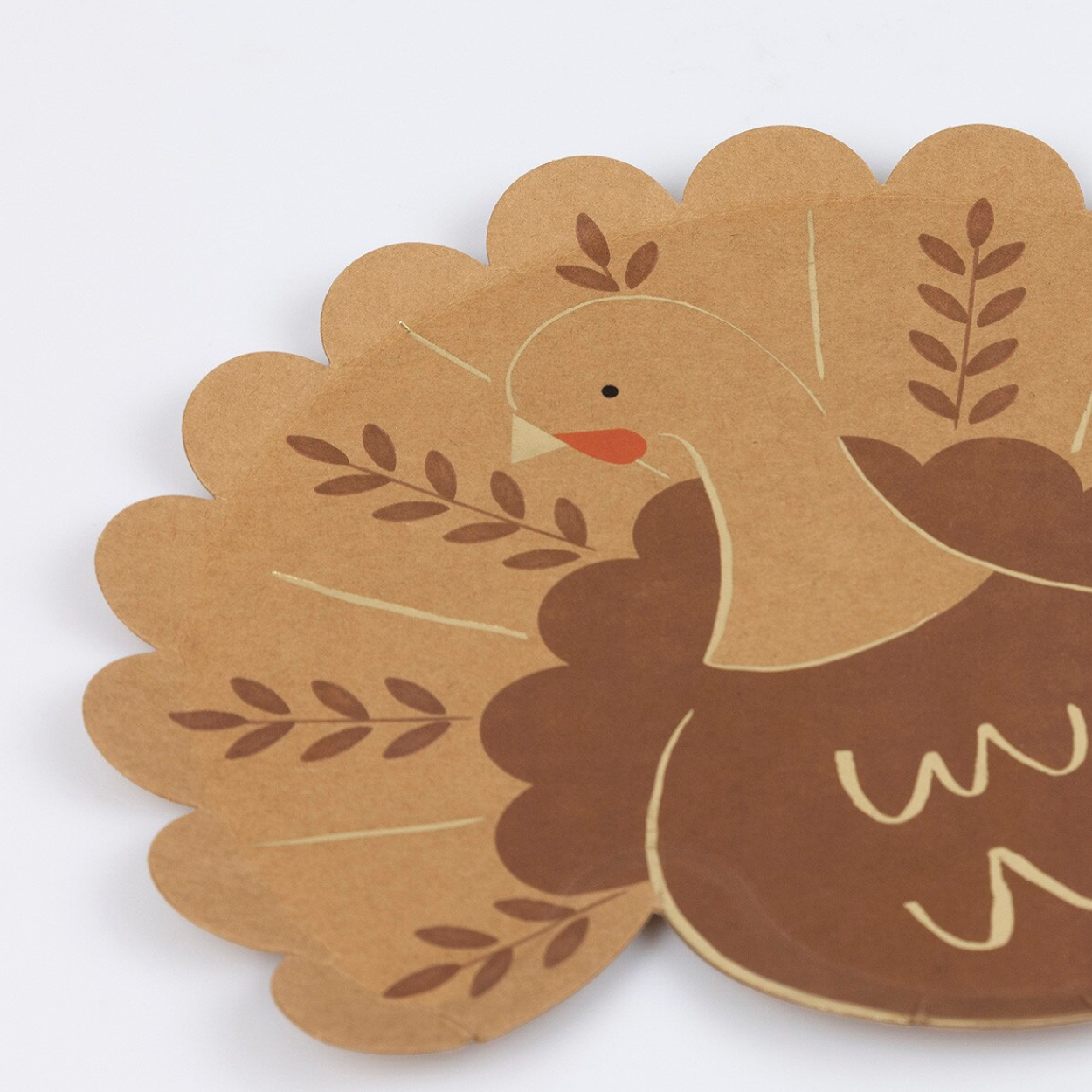 A close-up of a scalloped paper cutout featuring a turkey design in brown and tan with small orange beak details, photographed against a plain white background.