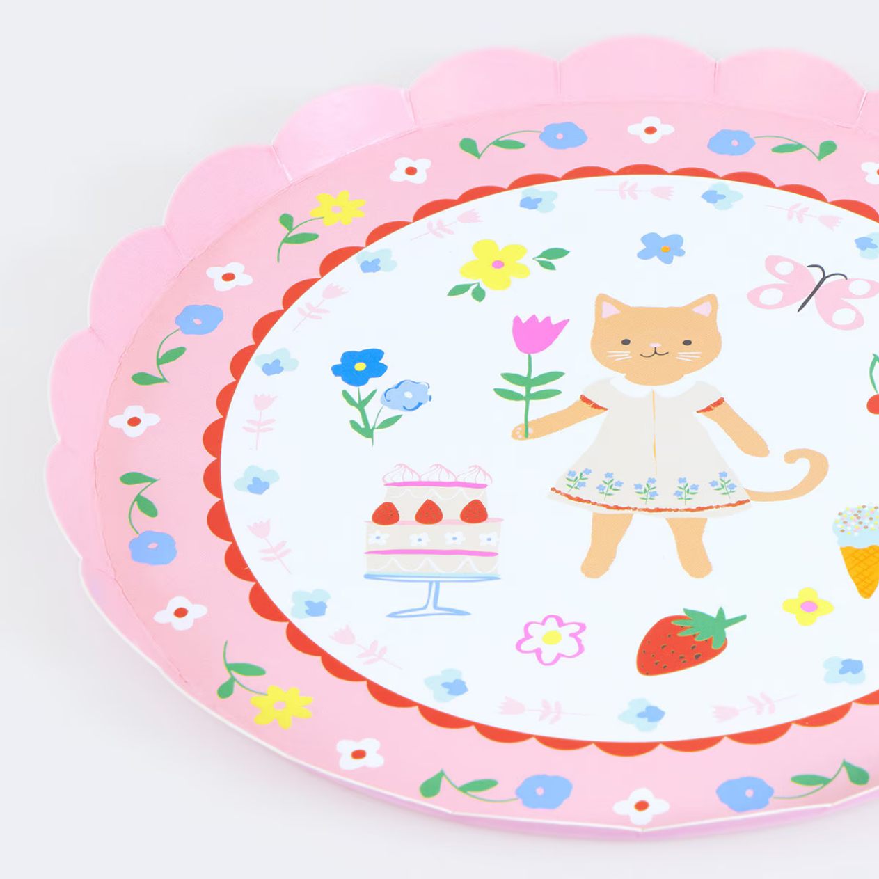 A scalloped pink paper plate featuring a cute cartoon cat in a white dress holding a flower, surrounded by colorful illustrations of flowers, a cake, a strawberry, and butterflies on a white background.