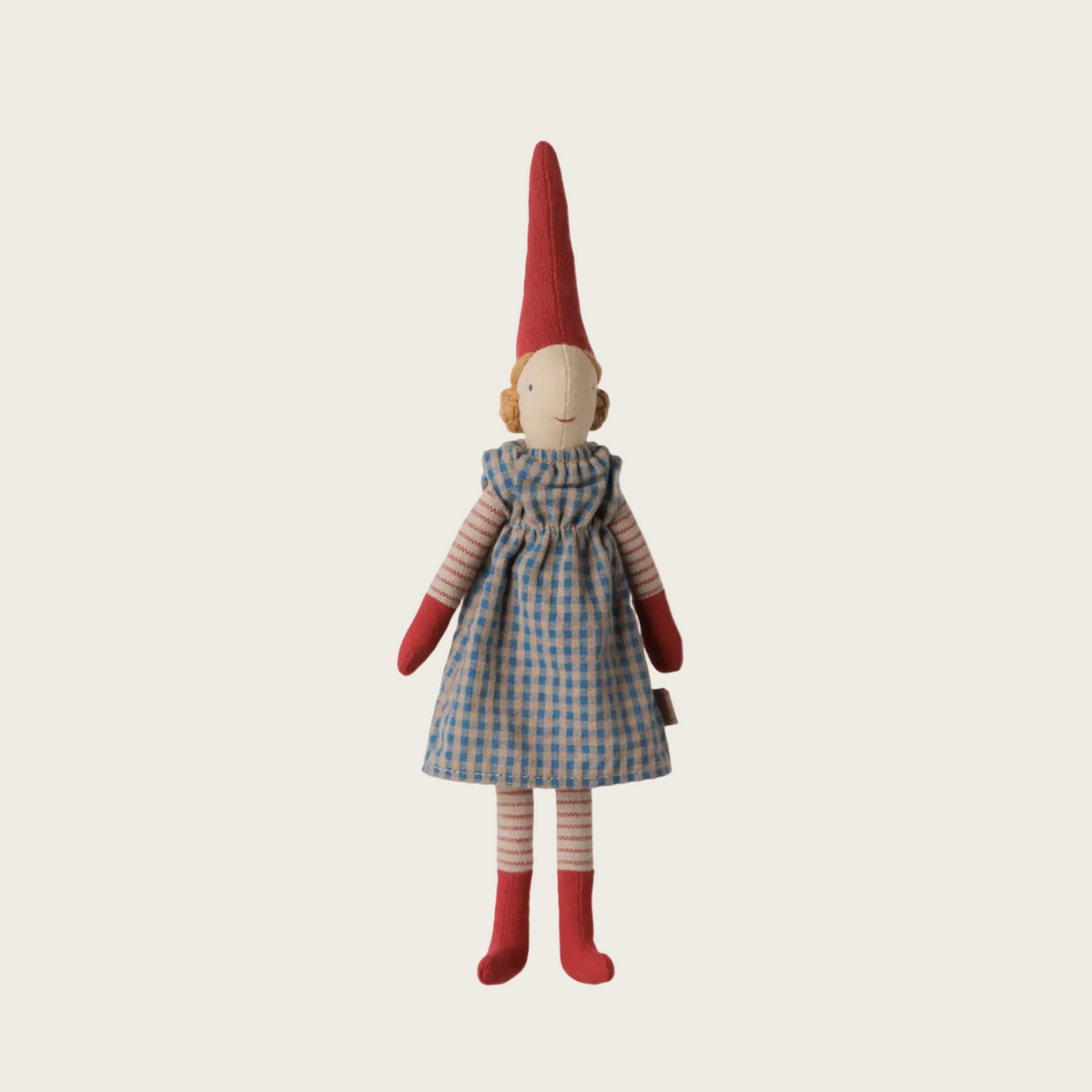 A handmade doll with a red pointed hat, a blue and white gingham dress, and red striped socks, under the brand name 'Maileg'.