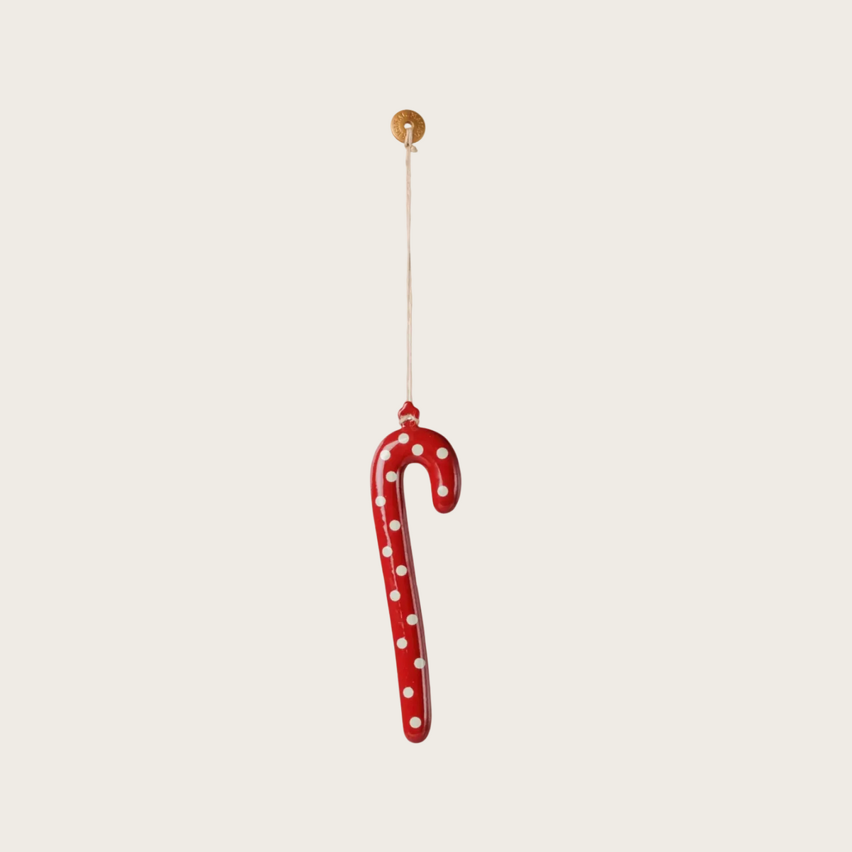 A red candy cane-shaped hanging ornament with white polka dots, suspended by a thin string from a gold button.