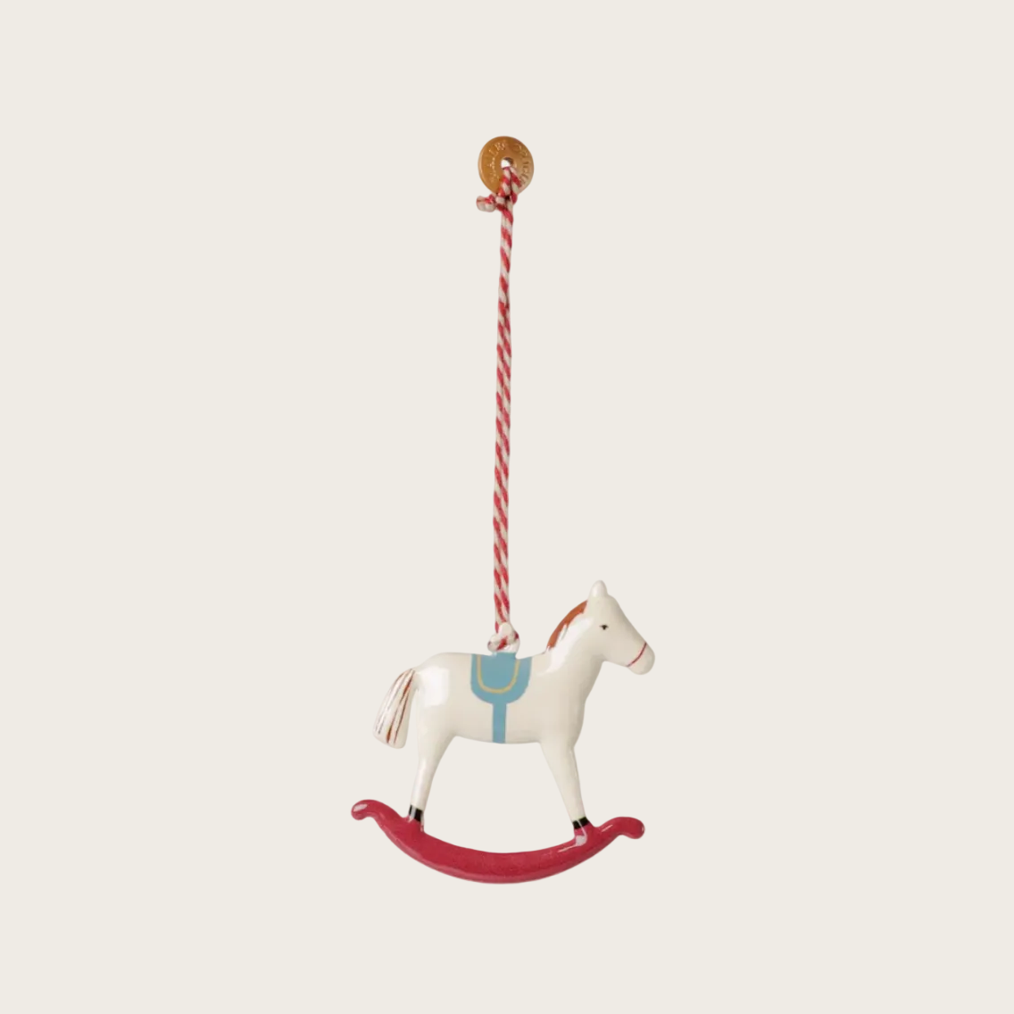 A small white rocking horse Christmas ornament with a red rocking base, blue saddle detail, and a red-and-white striped hanging string, shown against a plain light background.