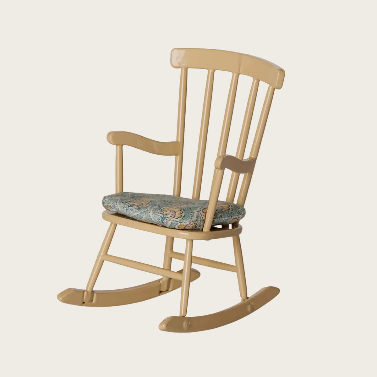 A light natural wood rocking chair with a patterned floral cushion. The chair features a spindle-back design with curved rockers and a cushioned seat.