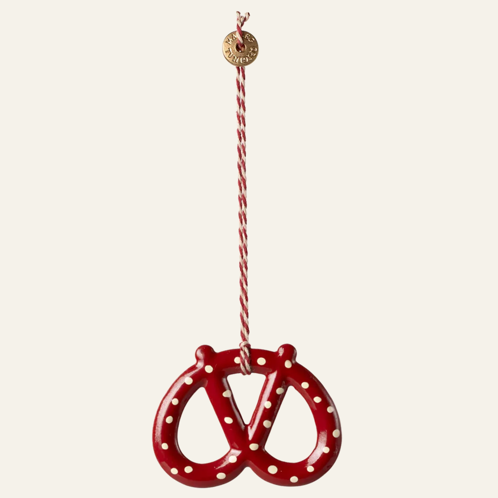 A red pretzel-shaped hanging ornament with white polka dots and a red-and-white striped hanging string, shown against a plain off-white background.