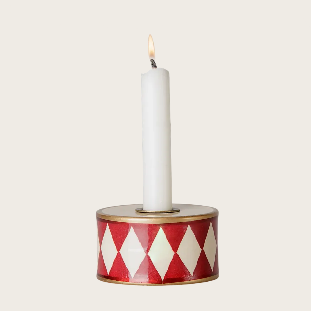 A candle holder drum with a red and white diamond pattern, holding a white taper candle.