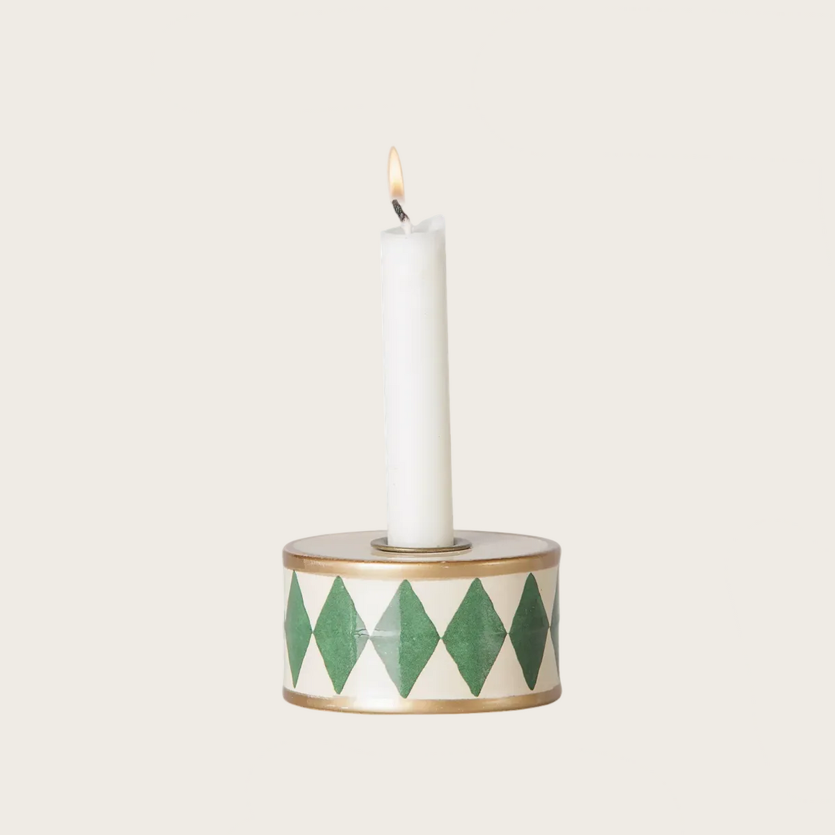 A candle holder drum with a green and white harlequin diamond pattern, holding a lit white taper candle.