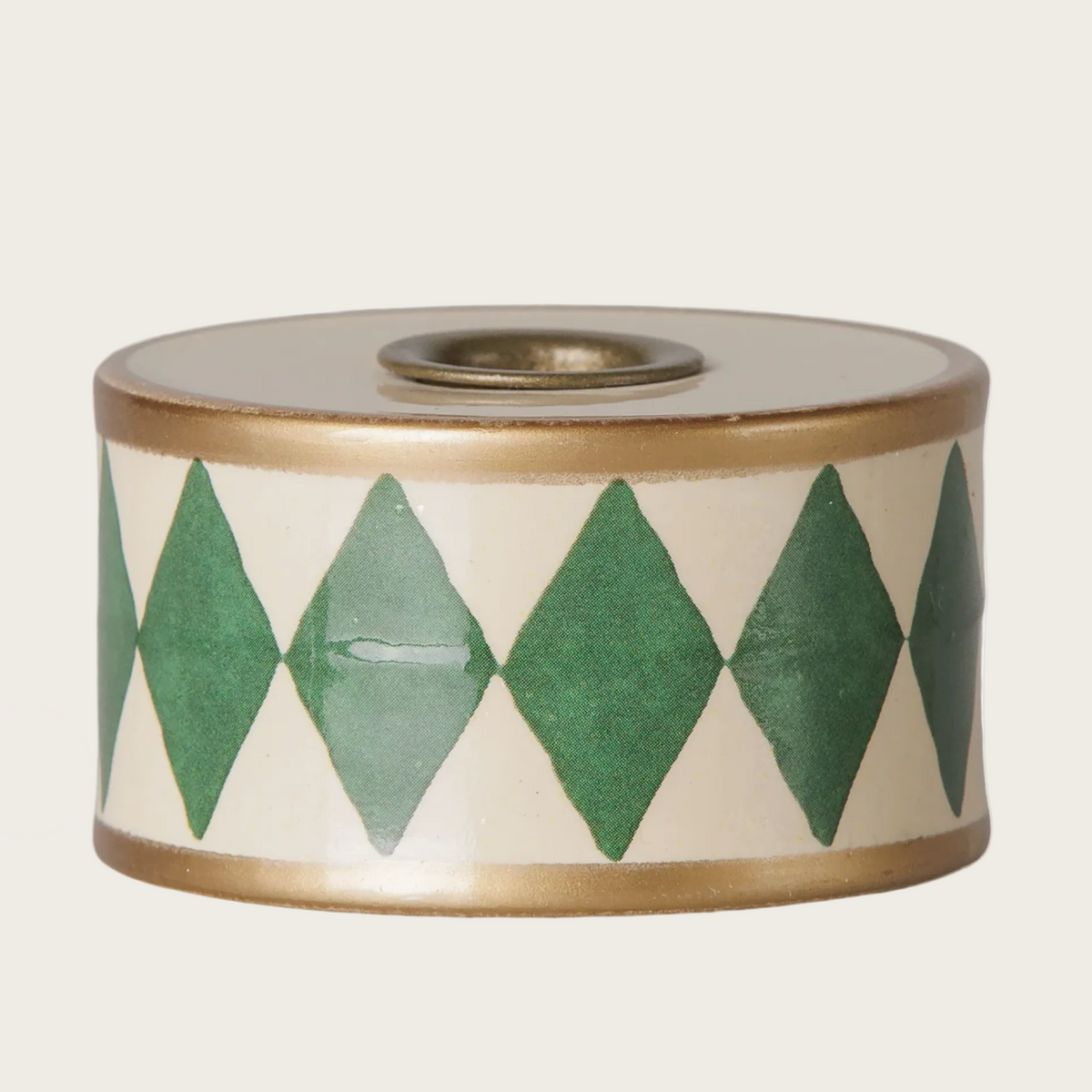 A close-up of a cylindrical candle holder with a cream-colored body, green diamond pattern, and a gold-toned rim.