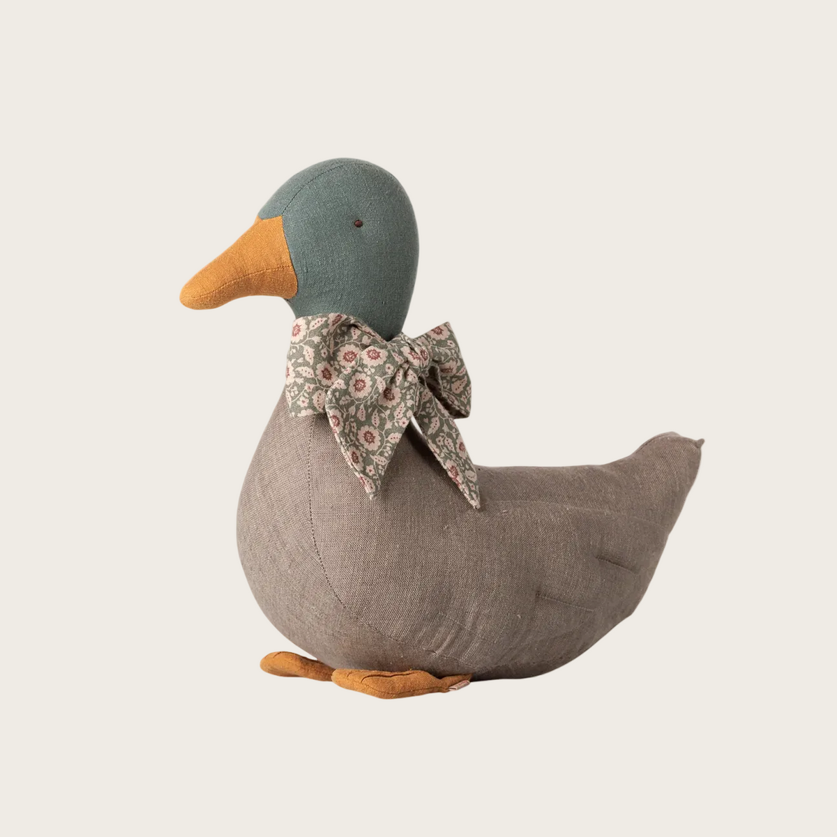 A plush duck toy in gray fabric with an orange beak and feet, wearing a patterned bow, shown on a white product page. 