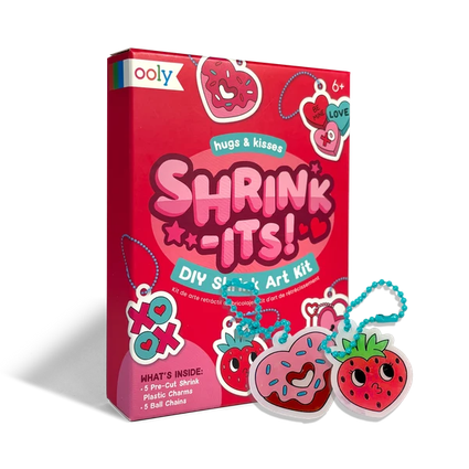 Ooly Shrink-Its! DIY Shrink Art Kit box in bright red, shown with two shrinkied plastic charms in front: a pink donut-shaped charm and a red strawberry-shaped charm, both attached to blue chains.