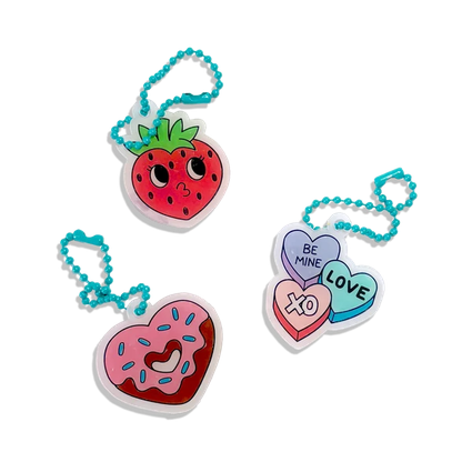 Three small acrylic keychain charms with turquoise bead chains on a plain white background: a strawberry charm, a pink donut charm, and a cluster of three heart charms reading "BE MINE," "LOVE," and "XD.".