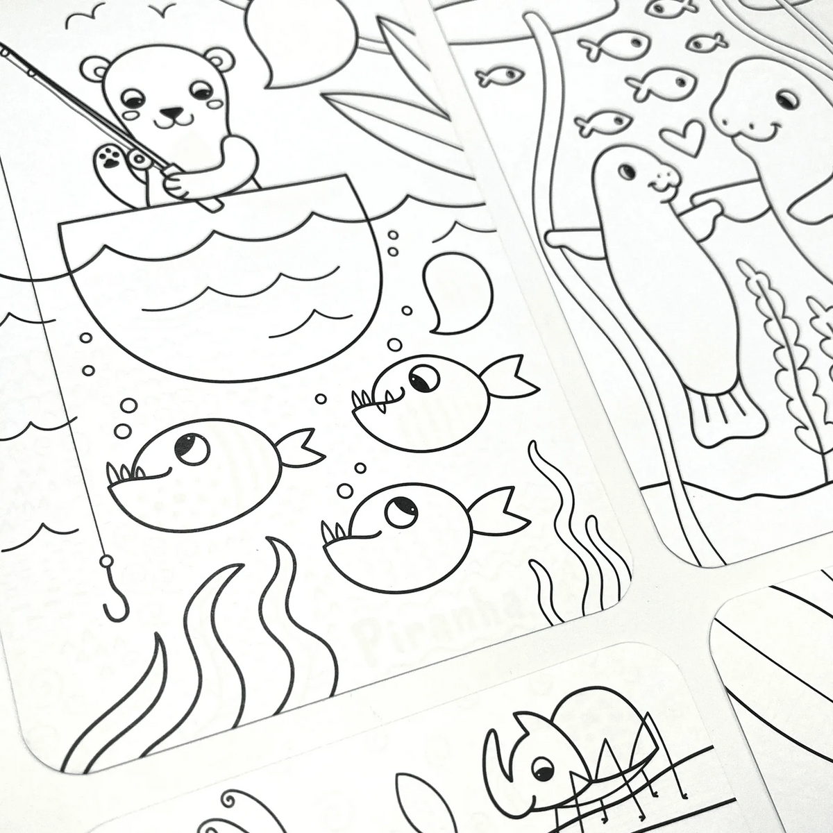 A close-up of several white cards or sheets printed with black line drawings of cute cartoon animals, including a bear fishing, fish, a seal, and a rhinoceros, arranged on a white surface.
