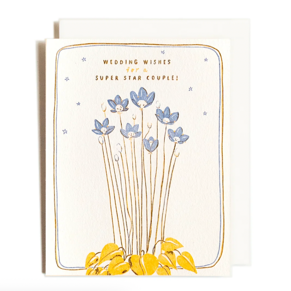 A greeting card from Press Studio featuring a whimsical illustration of blue flowers on tall stems rising from yellow leaves, with the text 'WEDDING WISHES FOR A SUPER STAR COUPLE!' on an off-white card with a matching envelope behind it.