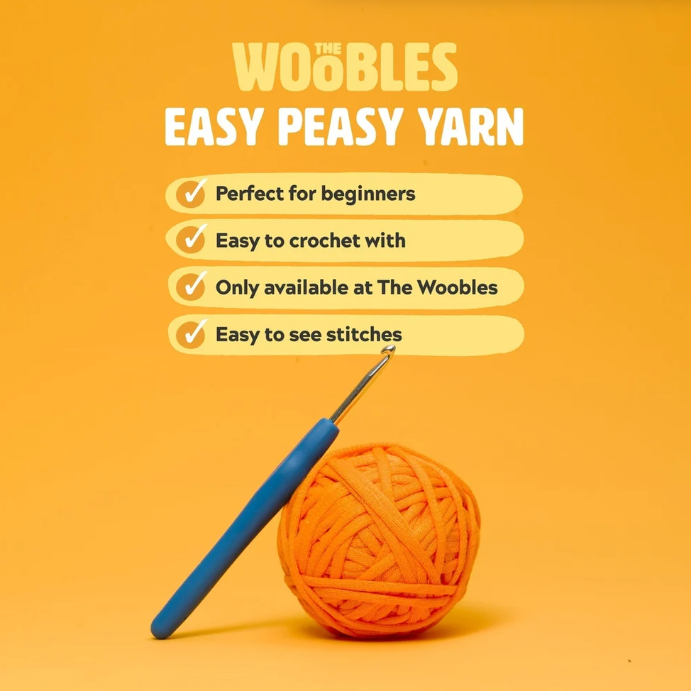 Promotional graphic for 'WOOBLES EASY PEASY YARN' on a bright yellow-orange background, featuring a blue-handled crochet hook and an orange ball of yarn with marketing text including 'Perfect for beginners' and 'Easy to crochet with.'.