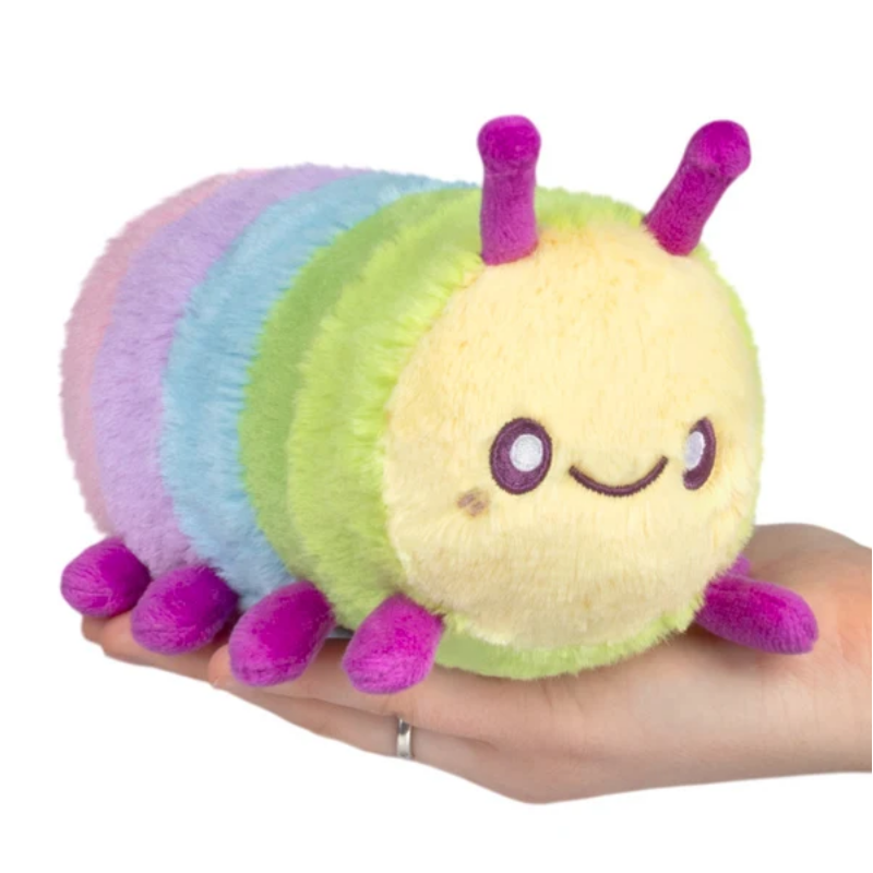 A plush caterpillar toy with pastel rainbow stripes and a yellow face, being held in a person's hand against a white background.