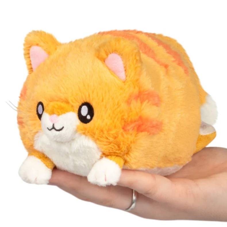 An orange and white fluffy cat plush toy being held in a person's hand against a plain white background.