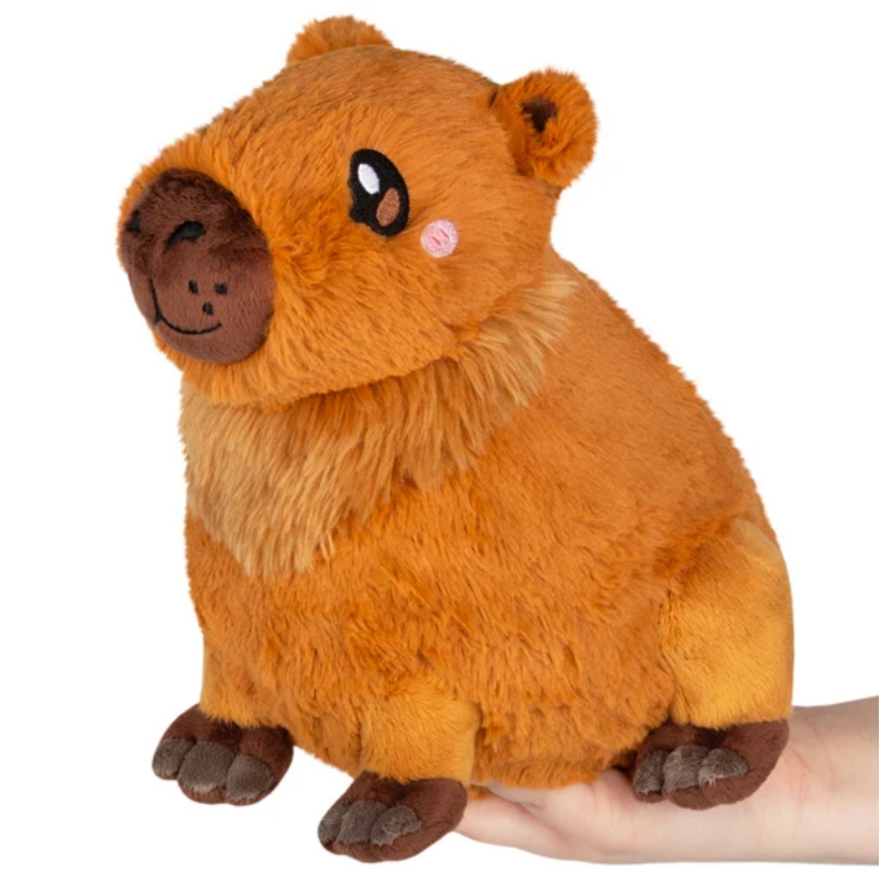 A plush capybara toy in warm orange-brown tones, being held by a person's hand against a plain white background.