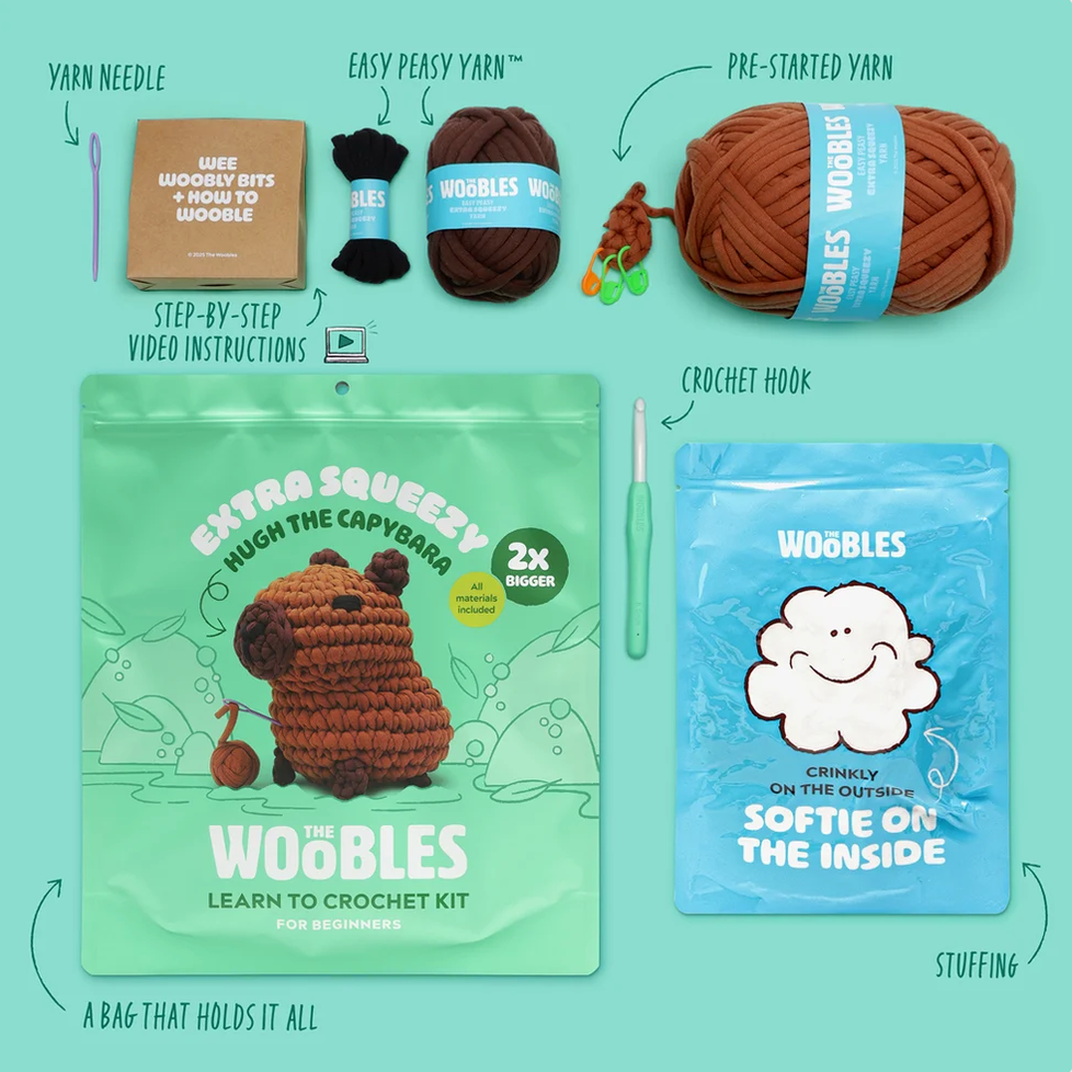 WooBles Learn to Crochet Kit contents arranged on a mint background: a yarn needle, easy peasy yarn ball, pre-started yarn ball, crochet hook, green Woobles extra squeeze bag, blue cloud stuffing bag, and a small crochet sample.
