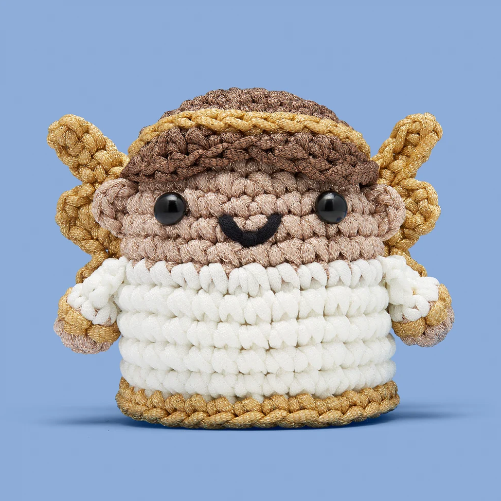 A crocheted plush toy with brown wings, a brown and beige headband, and a white body, shown against a solid blue background.