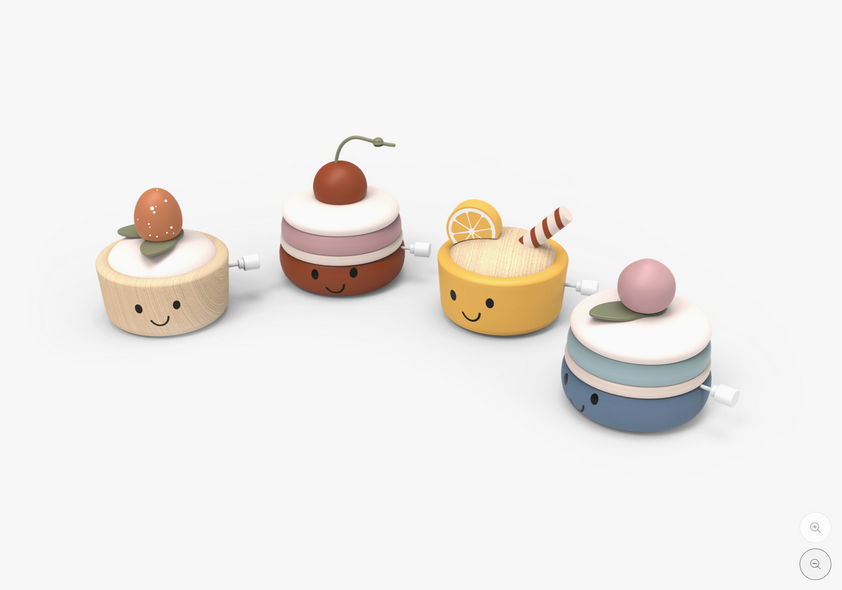 Four small wind-up toy cakes with smiling faces, arranged in a row on a clean white background. The cakes are decorated with colorful tops and have visible winding keys on the sides.
