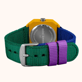A close-up of a watch from the back, showing a bright yellow case and a multi-colored woven strap in green, blue, and purple with a silver buckle.