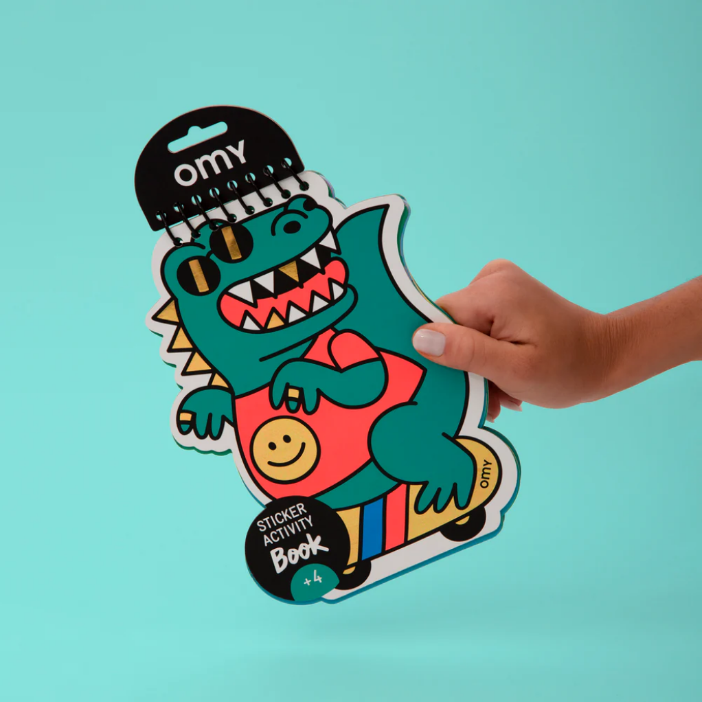 A hand holding a sticker book with a colorful dinosaur character on the cover.