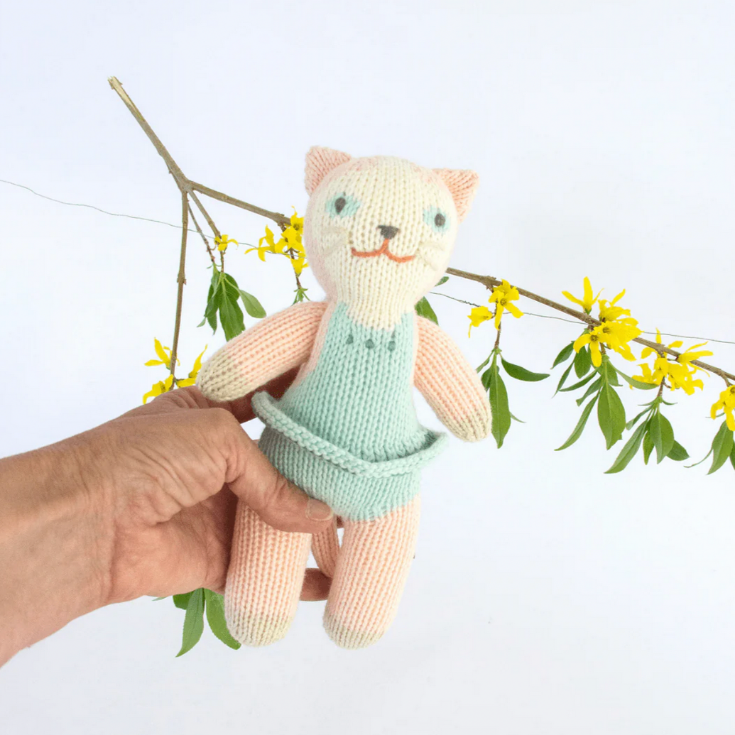 Handmade cat toy in a light green outfit held by a hand with a branch and yellow flowers in the background.