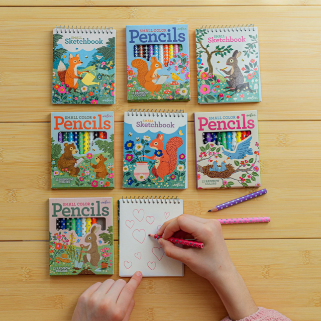 Colorful children's sketchbooks and pencils on a wooden surface with a hand drawing.