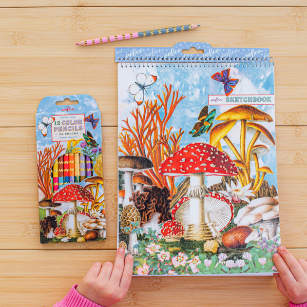 Children's art supplies including a colorful sketchbook with a mushroom design on a wooden table.