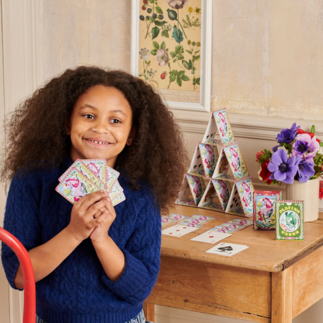 Child playing with colorful cards in a room with a wooden table and decorative items.