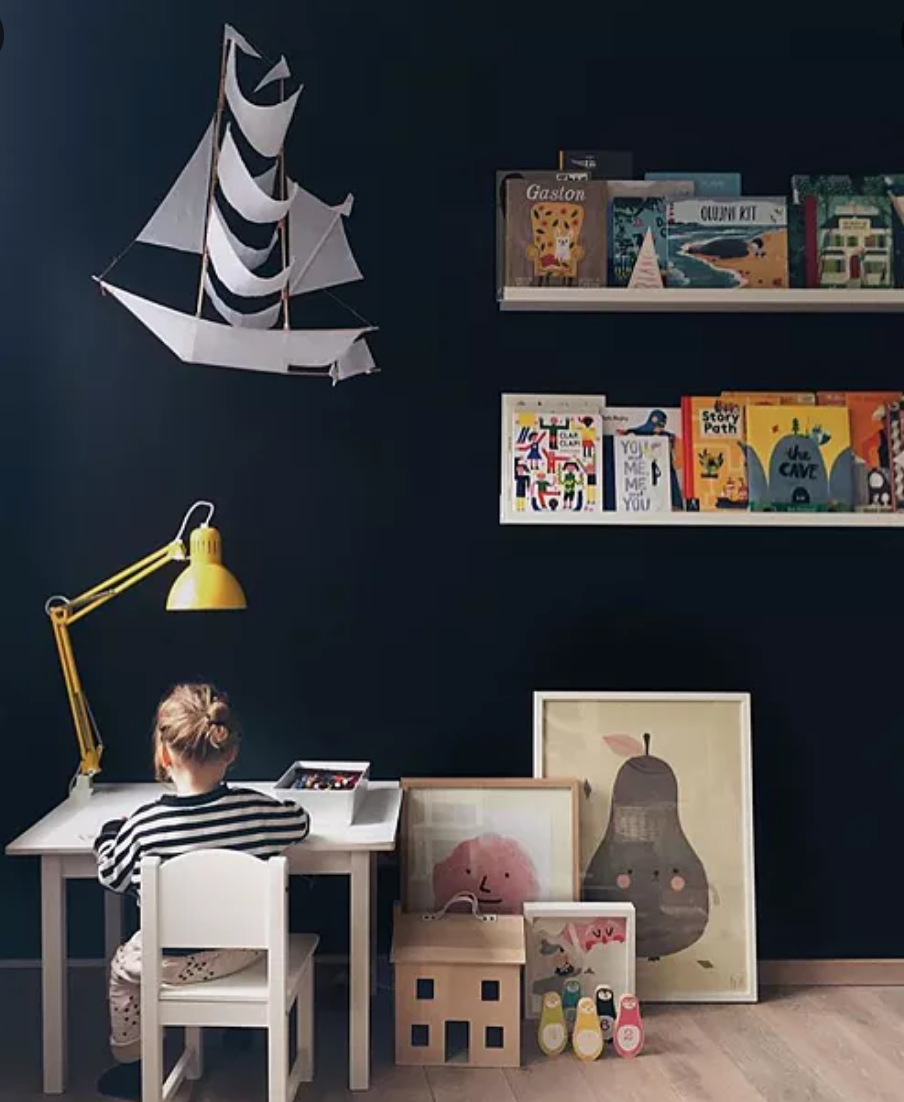 Child sitting at a desk in a room with dark walls, colorful books, and decorative items.